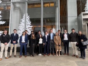 Many students wearing formal attire stand in front of a large window